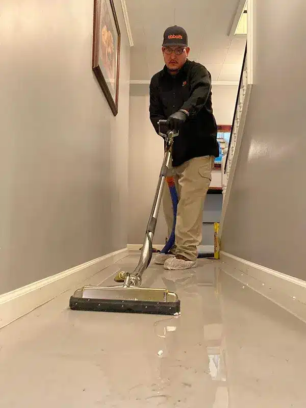 Technician using a water extraction tool on a flooded hallway floor